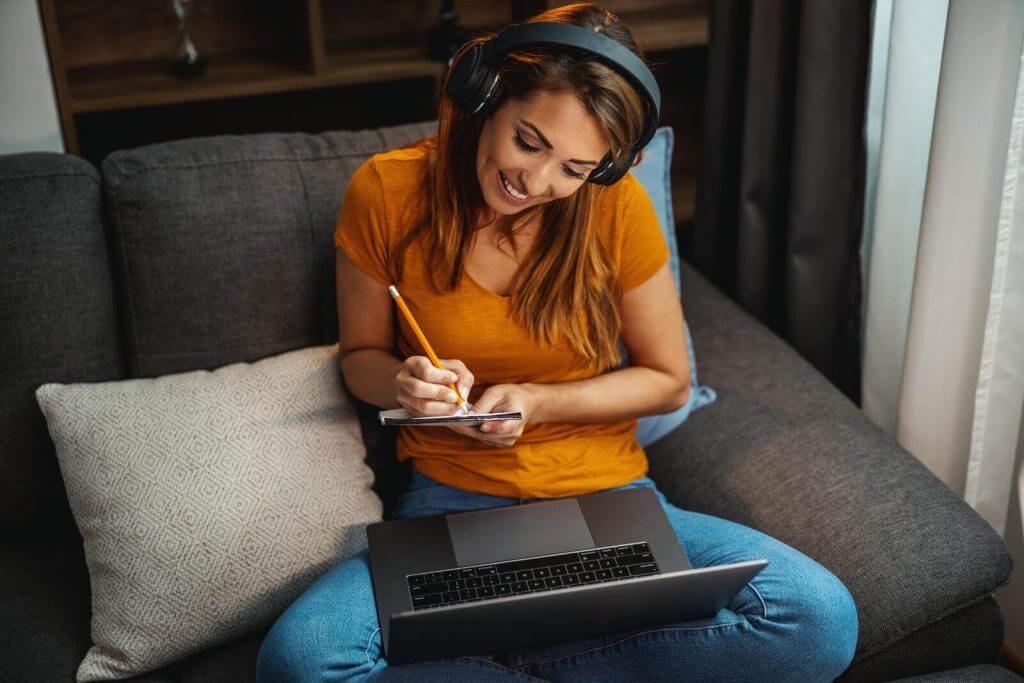 A woman sitting on a couch with headphones and a laptop