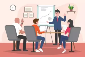 A business meeting with four people: one presenting by a chart, others seated with laptops and papers. A wall clock, frames, and a plant decorate the room.