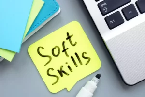 Yellow sticky note with "Soft Skills" written on it next to a black marker and a laptop keyboard.