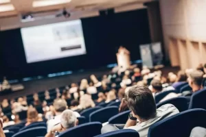 People sitting in an auditorium watching a presentation on a large screen.