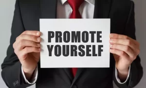 A person in a suit holds a sign that reads "PROMOTE YOURSELF" in bold letters.