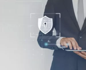 A person in a suit uses a tablet with a digital security graphic overlay, featuring a shield and keyhole symbol, suggesting data protection.