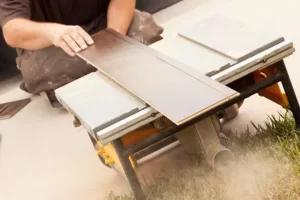 A person using a table saw to cut a wooden plank outdoors.