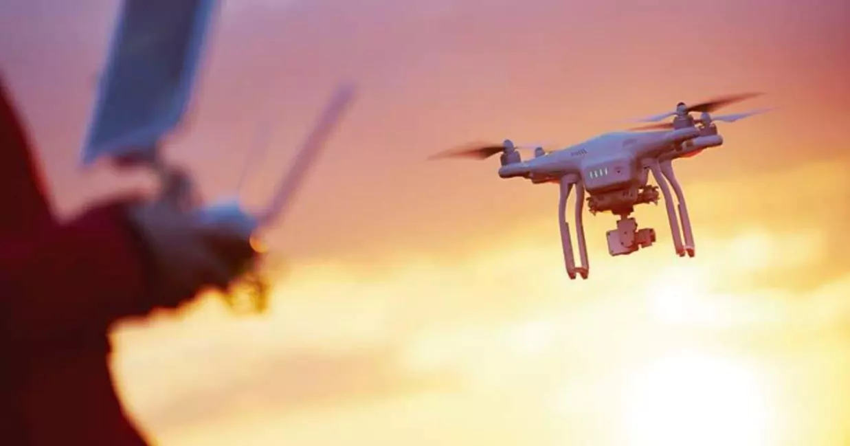 A person operates a drone with a remote control against a sunset sky.