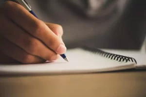 A person writes on a spiral-bound notebook with a pen.