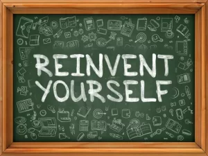 A chalkboard with "Reinvent Yourself" written in large white letters, surrounded by doodles of books, calculators, and other stationery items.