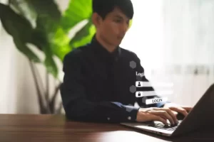 Person in a dimly lit room using a laptop with a login interface overlay.