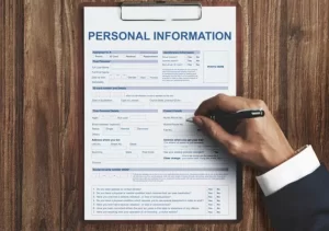 A person fills out a personal information form on a clipboard with a pen.