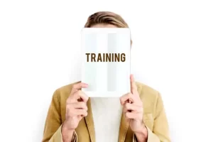 Person holding a tablet covering their face. The tablet displays the word "TRAINING" in bold letters.